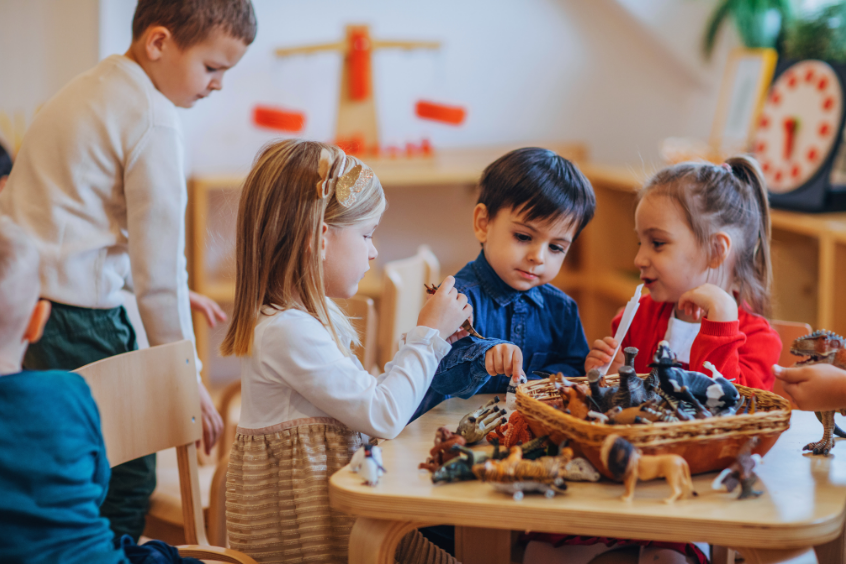 Group of young children playing together with animal figures at a table in a preschool classroom