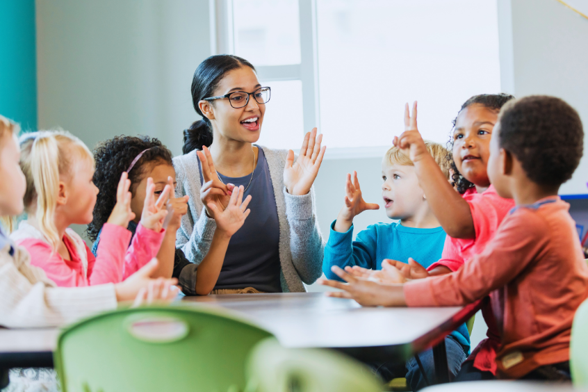Teacher sitting with a diverse group of young children at a table during a classroom activity 