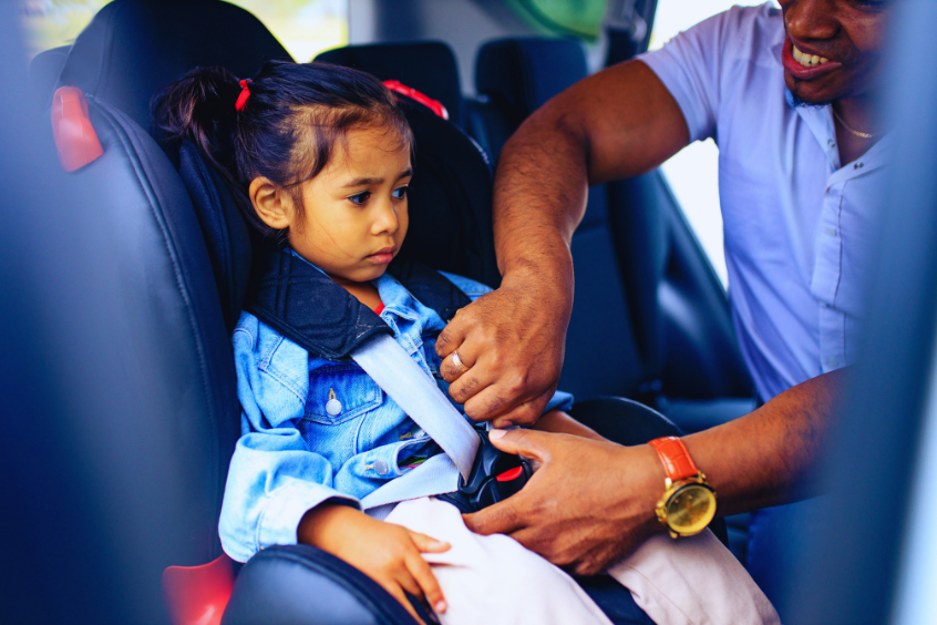 Parent securing their young child in their car seat before a car ride. 